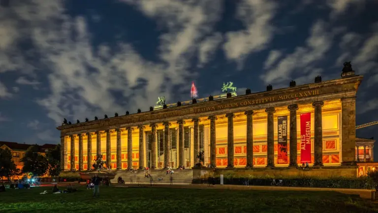 Die beleuchtete Museumsinsel in Berlin bei Nacht mit wolkigem Himmel im Hintergrund.