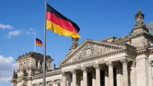 Deutscher Reichstag in Berlin mit wehender deutscher Flagge bei Tageslicht.
