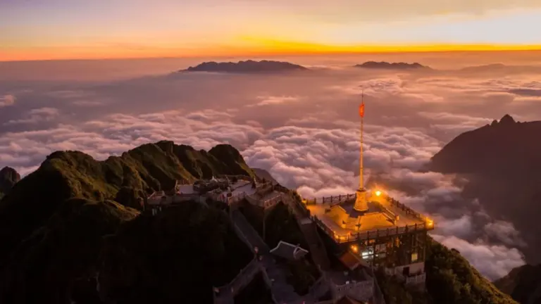 Blick auf ein beleuchtetes Gebäude in den Bergen bei Sonnenaufgang über den Wolken.