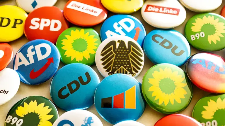 Bunte Anstecknadeln verschiedener deutscher politischer Parteien liegen auf einem Tisch verteilt.