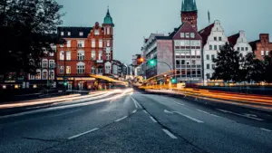 Lübecker Stadtkulisse bei Nacht mit beleuchteten Gebäuden und vorbeifahrenden Autos.