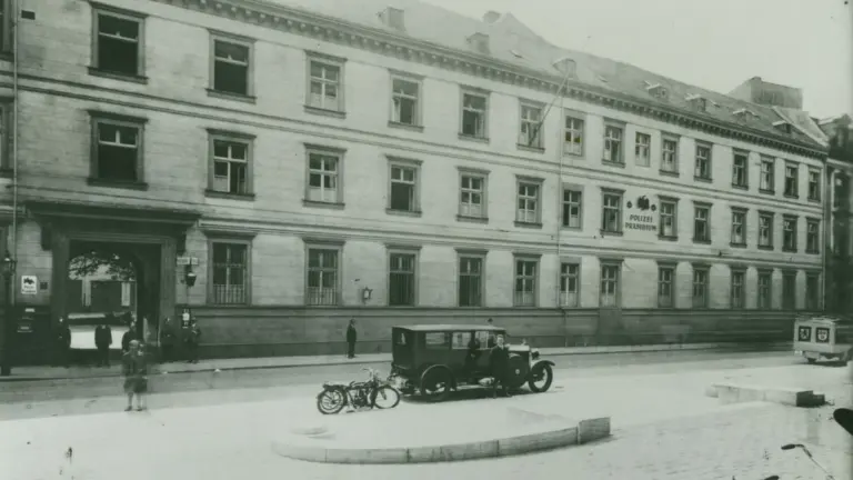Historisches Gebäude des Polizeipräsidiums mit altem Automobil und Motorrad auf einem gepflasterten Platz.