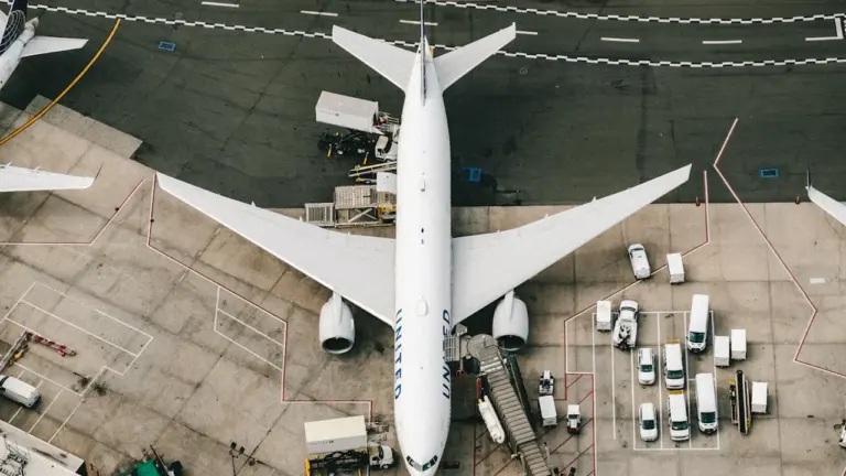 Ein weißes Passagierflugzeug steht bei Tageslicht am Flughafen zur Abfertigung bereit.