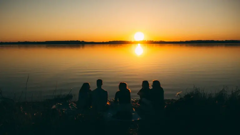 Eine Gruppe von Freunden genießt gemeinsam den friedlichen Sonnenuntergang an einem See bei Leipzig.
