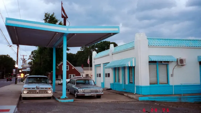 Vintage Tankstelle mit klassischen Autos unter einem blauen Vordach an einem Tag.
