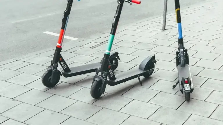 Drei E-Scooter stehen ordentlich nebeneinander auf einem grauen Gehweg in einer europäischen Stadt.