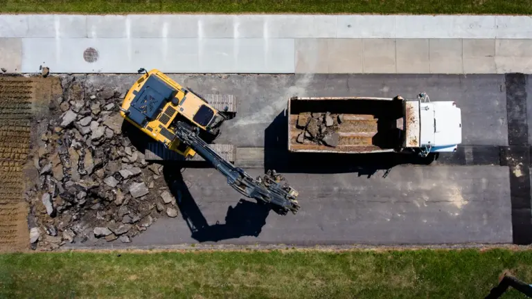 Draufsicht auf einen Bagger bei Straßenbauarbeiten und Asphaltentsorgung auf einer Baustelle.