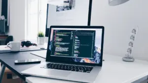 Ein sauberer Schreibtisch mit einem Laptop, auf dessen Bildschirm Programmcode zu sehen ist.