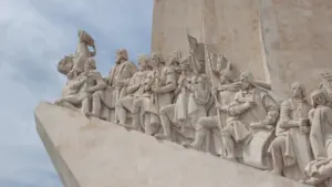 Monumentale Steinskulptur historischer Figuren auf einem schiffsförmigen Denkmal unter bewölktem Himmel.