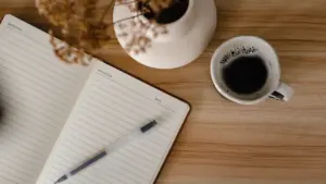 Notizbuch mit Stift und Kaffeetasse auf einem Holztisch für morgendliche Planung.