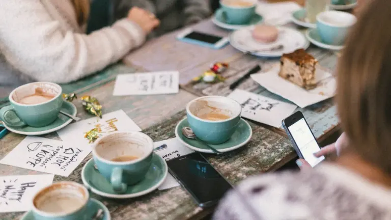 Freunde sitzen in einem Berliner Café an einem Tisch mit Kaffeetassen und Smartphones.