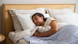 Eine junge Frau schläft friedlich in einem Bett mit heller Bettwäsche und Decke.