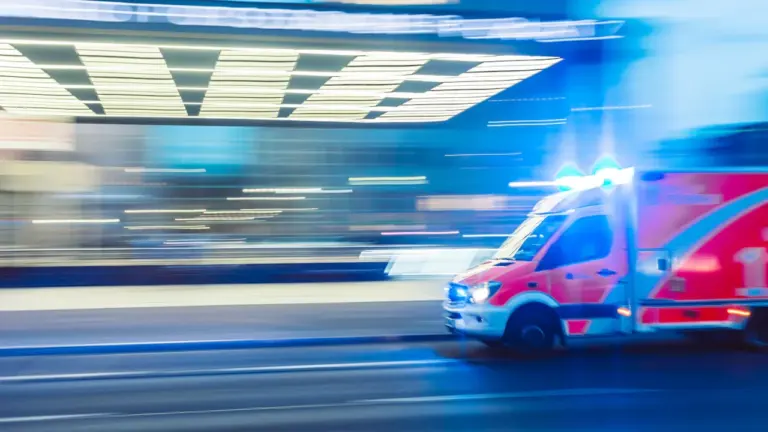 Ein Rettungswagen fährt nachts mit Blaulicht durch eine deutsche Stadt.