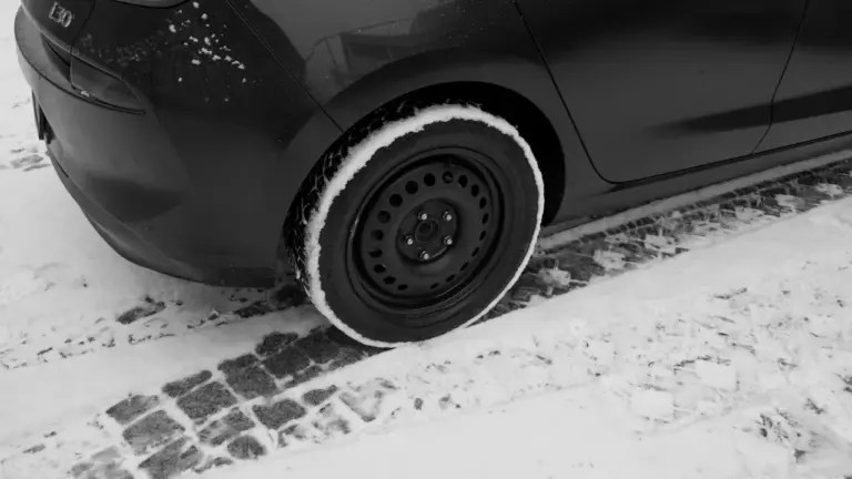 Ein Autoreifen auf einer verschneiten Straße mit Kopfsteinpflaster bei winterlichem Wetter.