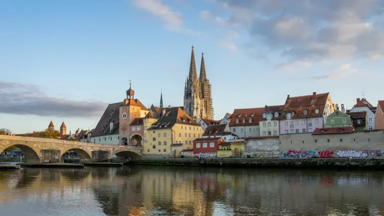 Blick auf den Regensburger Dom mit historischen Gebäuden entlang der Donau bei Tageslicht.