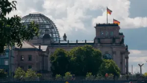 Das Reichstagsgebäude in Berlin mit wehenden deutschen Flaggen vor blauem Sommerhimmel.