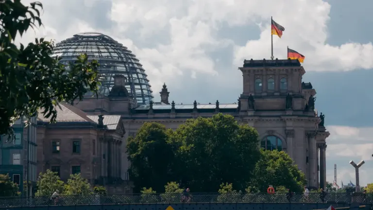 Das Reichstagsgebäude in Berlin mit wehenden deutschen Flaggen vor blauem Sommerhimmel.