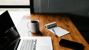 Laptop mit Kaffeetasse und Notizblock auf einem dunklen Holztisch für fokussiertes Arbeiten.