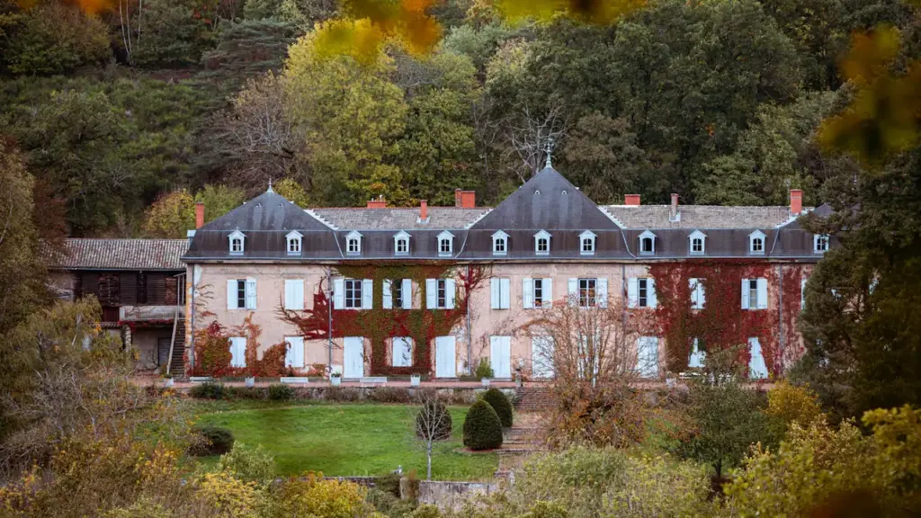 Ein weißes Wohnhaus umgeben von herbstlichen Bäumen mit gefallenen Blättern im Vorgarten.