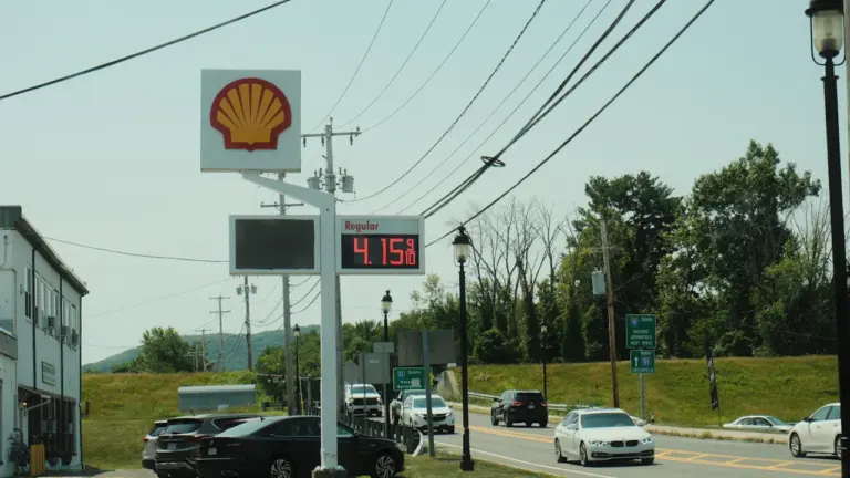 Eine Shell Tankstelle mit Preisanzeige und vorbeifahrenden Autos bei Tageslicht.