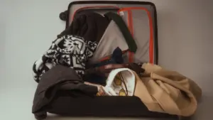 Ein offener, überquellender Koffer mit verschiedenen Kleidungsstücken symbolisiert Reisevorbereitung und persönliche Last.